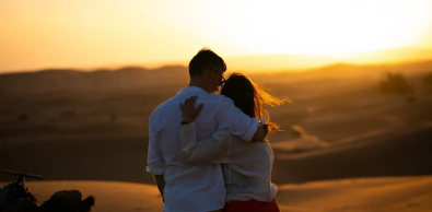 Couple hugging and watching the sunset over the Sahara dunes during a romantic Merzouga tour in Morocco.